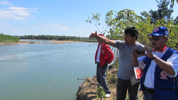 Medewerkers van het lokale Rode Kruis bekijken de situatie vanaf de oever van een rivier.